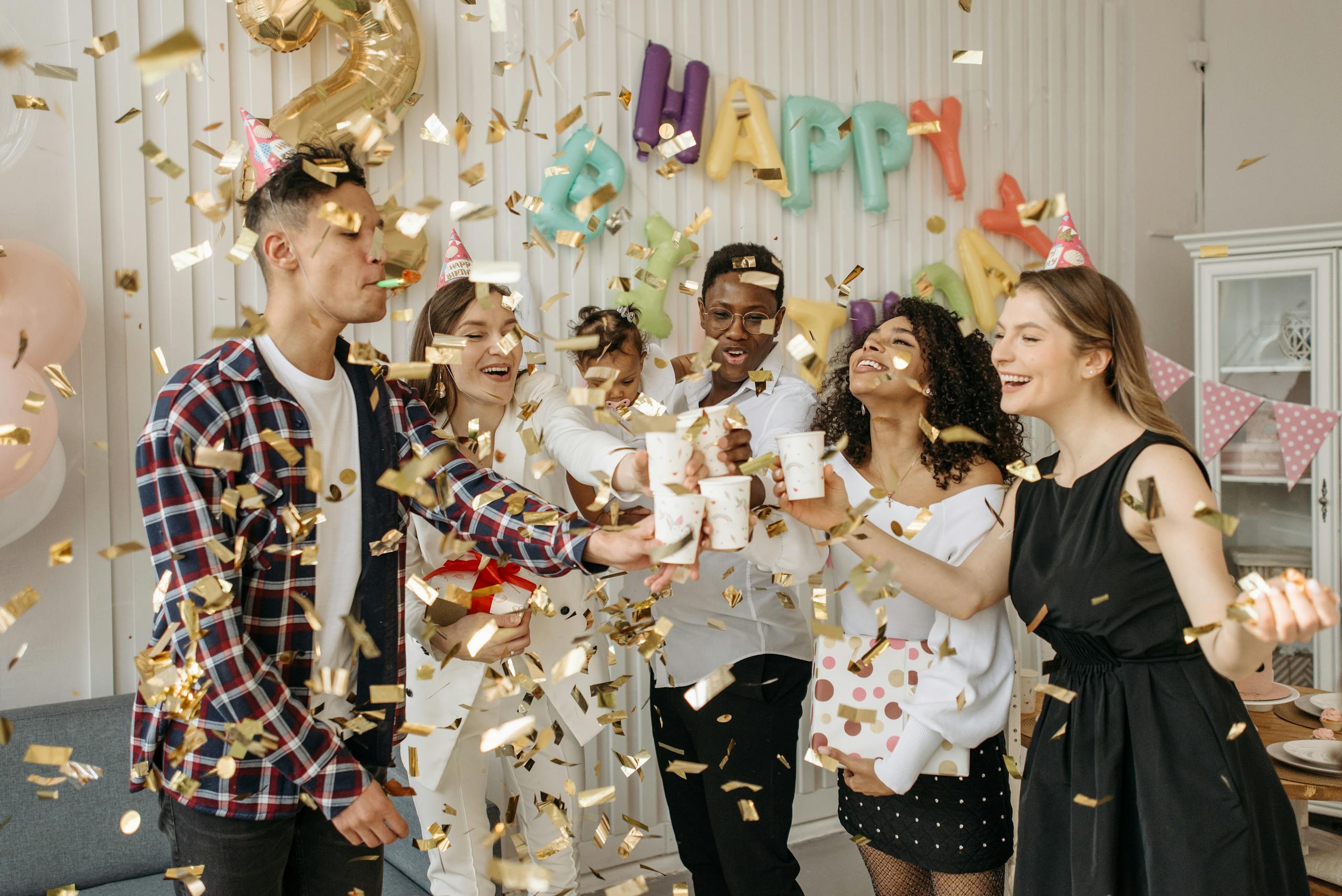 A lively indoor birthday party with friends celebrating with confetti and drinks in a decorated room.